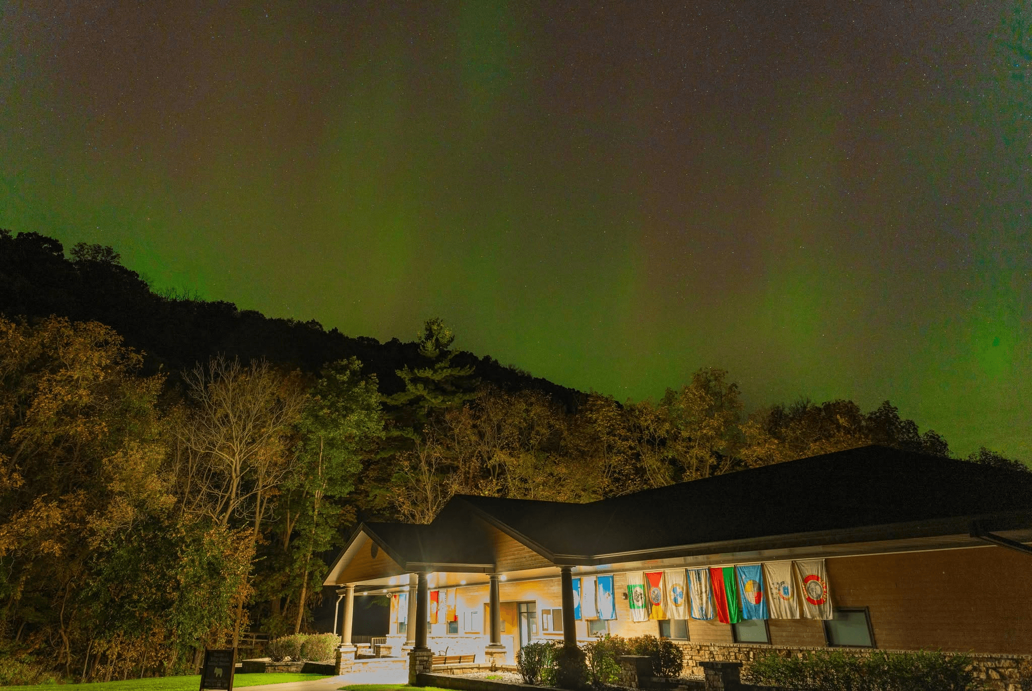 A building with flags hanging outside it with a vibrant display of the aurora borealis above.