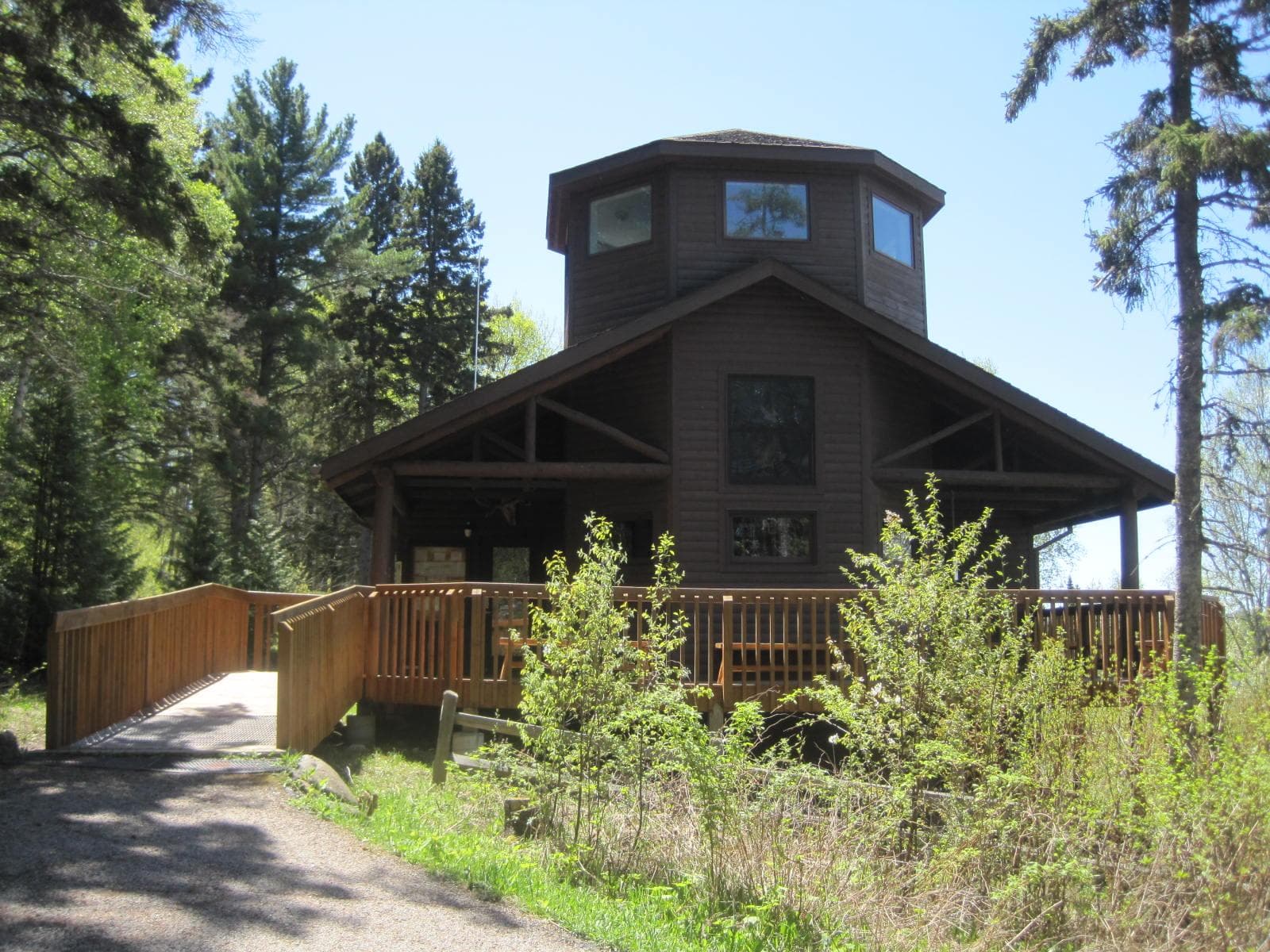 A brown building with a ramp leading to it is surrounded by green vegetation.