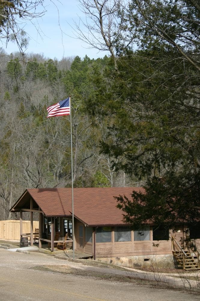 A brown building with an American Flag flying in front. Trees are visible behind the store.