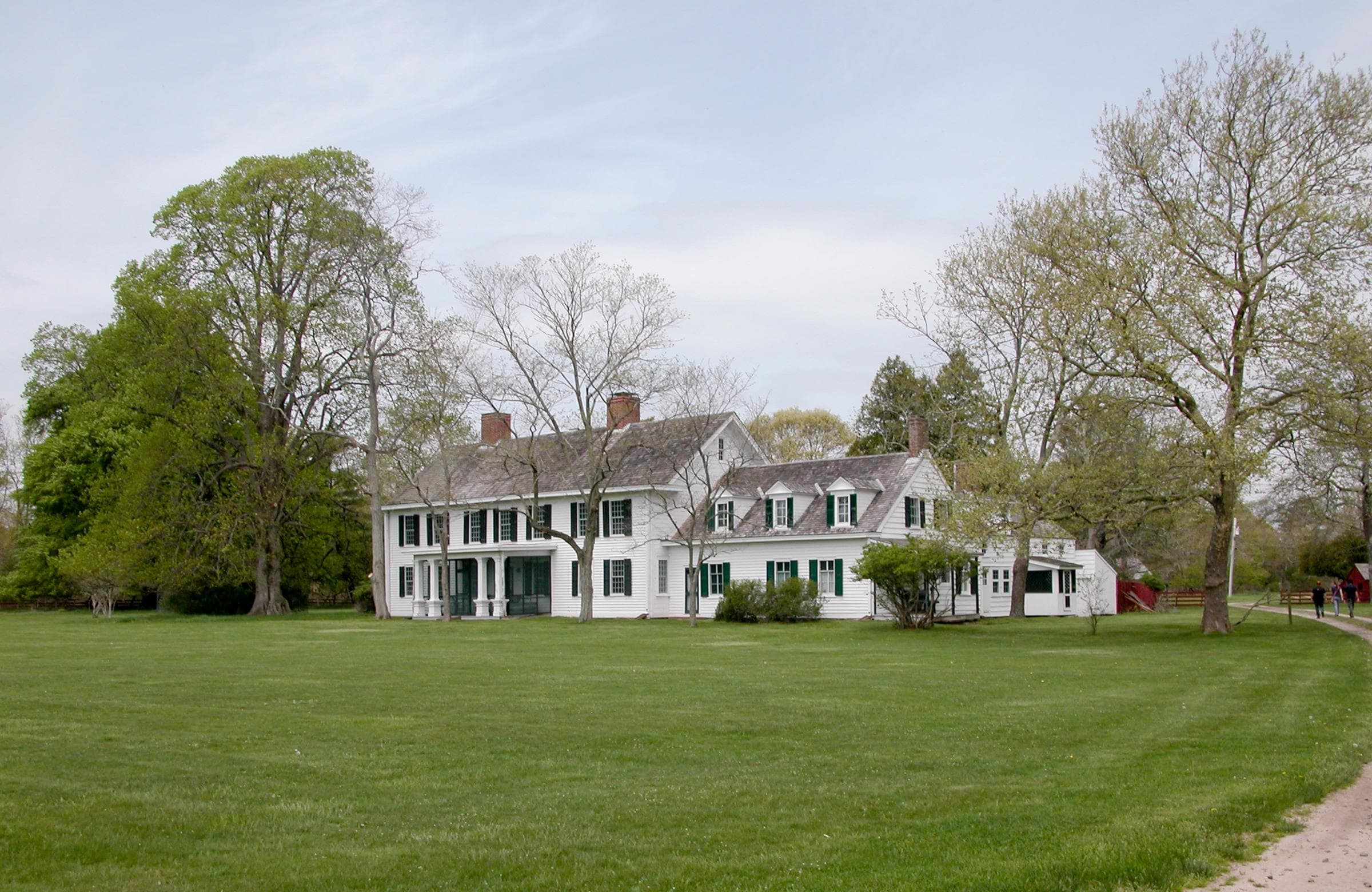 A large colonial manor is surrounded by green grass and trees.