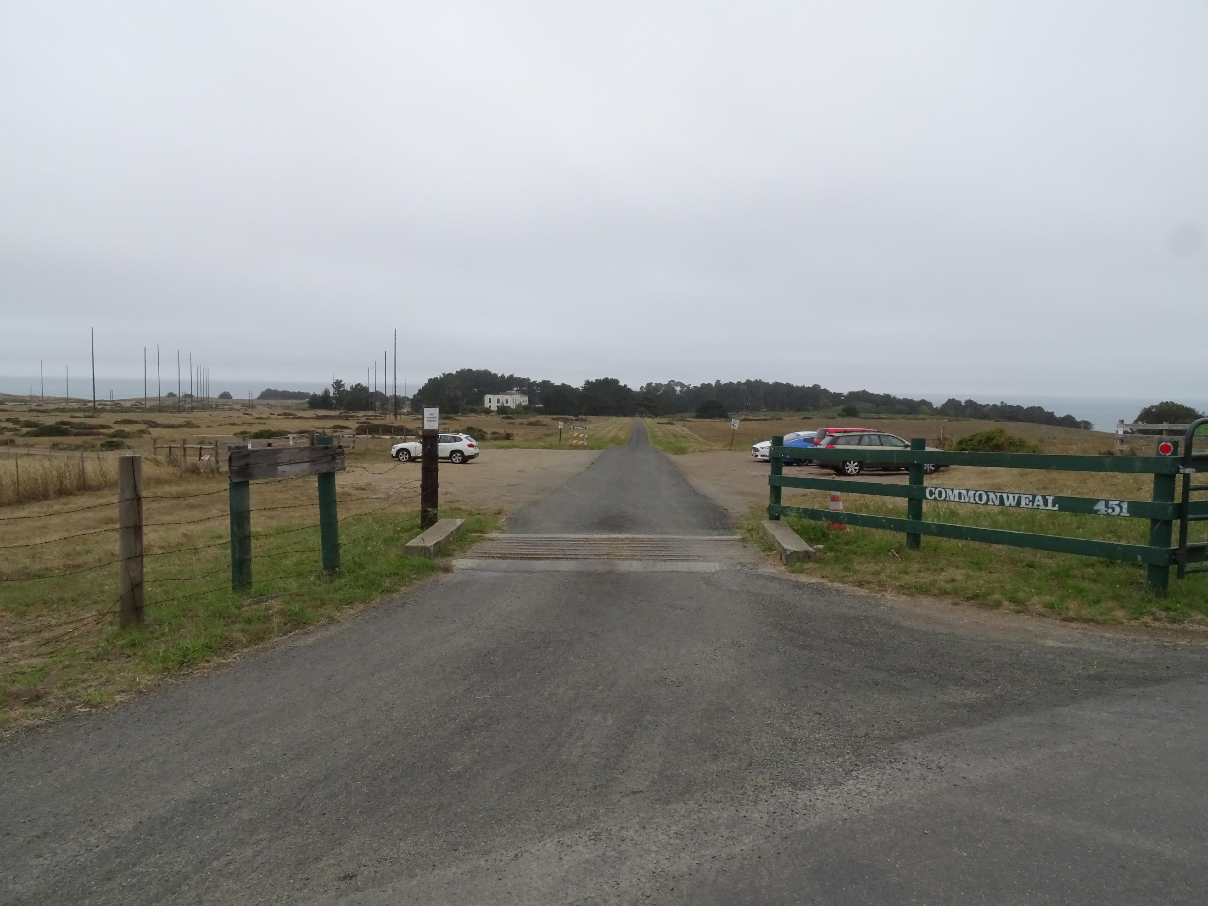 Five vehicles in a small dirt/gravel parking lot beyond a cattle guard and a green fence.