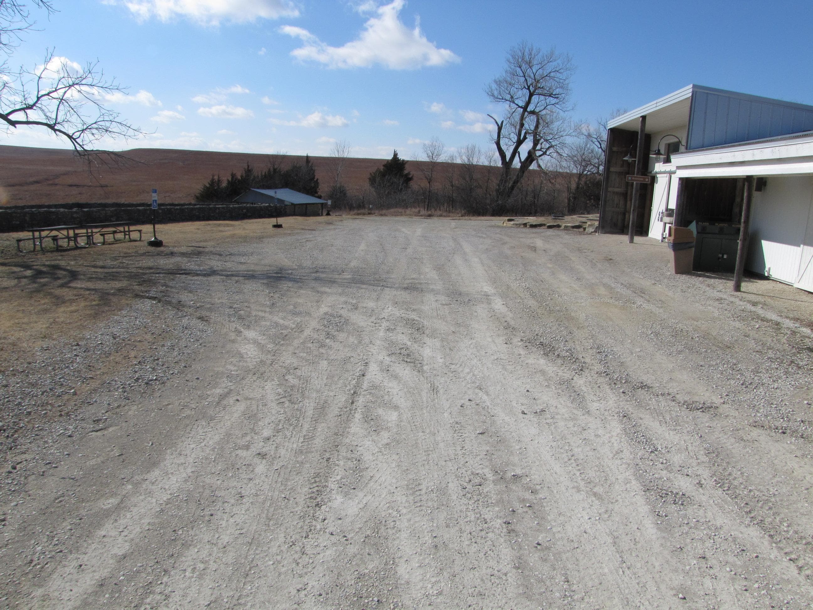 A wide gravel road with picnic tables to the left and buildings to the right.