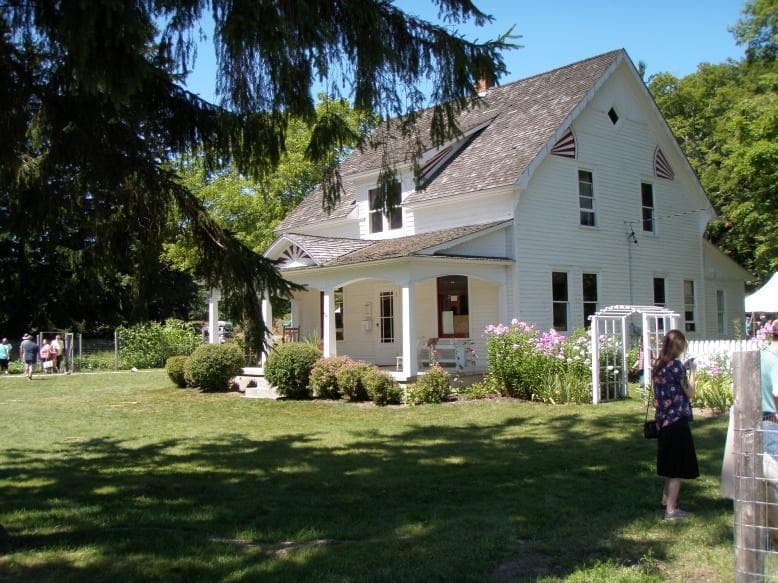Corner view of white, clapboard house with large, gabled, front porch and side garden trellis