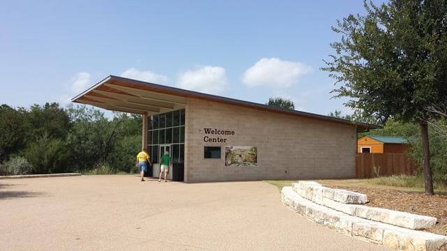Two people enter a small, brick building labeled "Welcome Center"