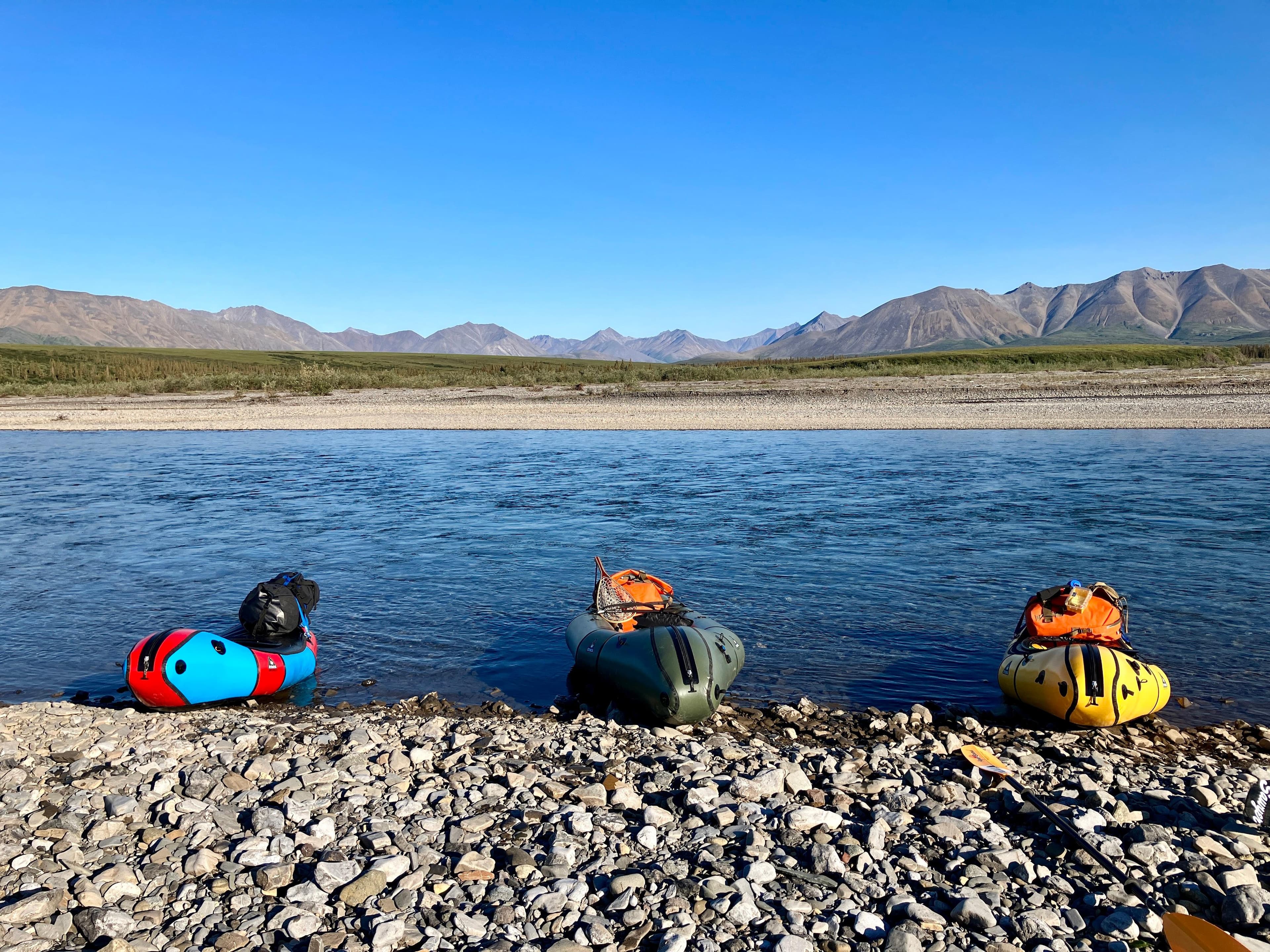 Three multicolored packrafts on the gravel shore of the Kelly river