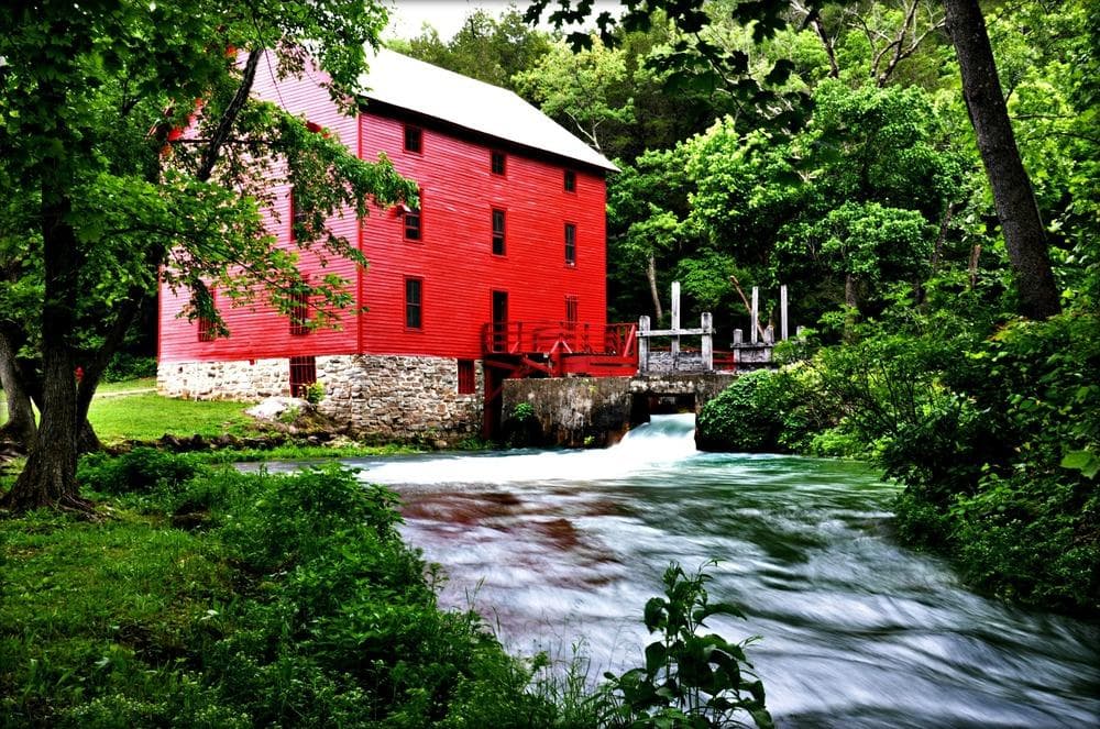 Red Alley Mill with green foliage and blue water flowing