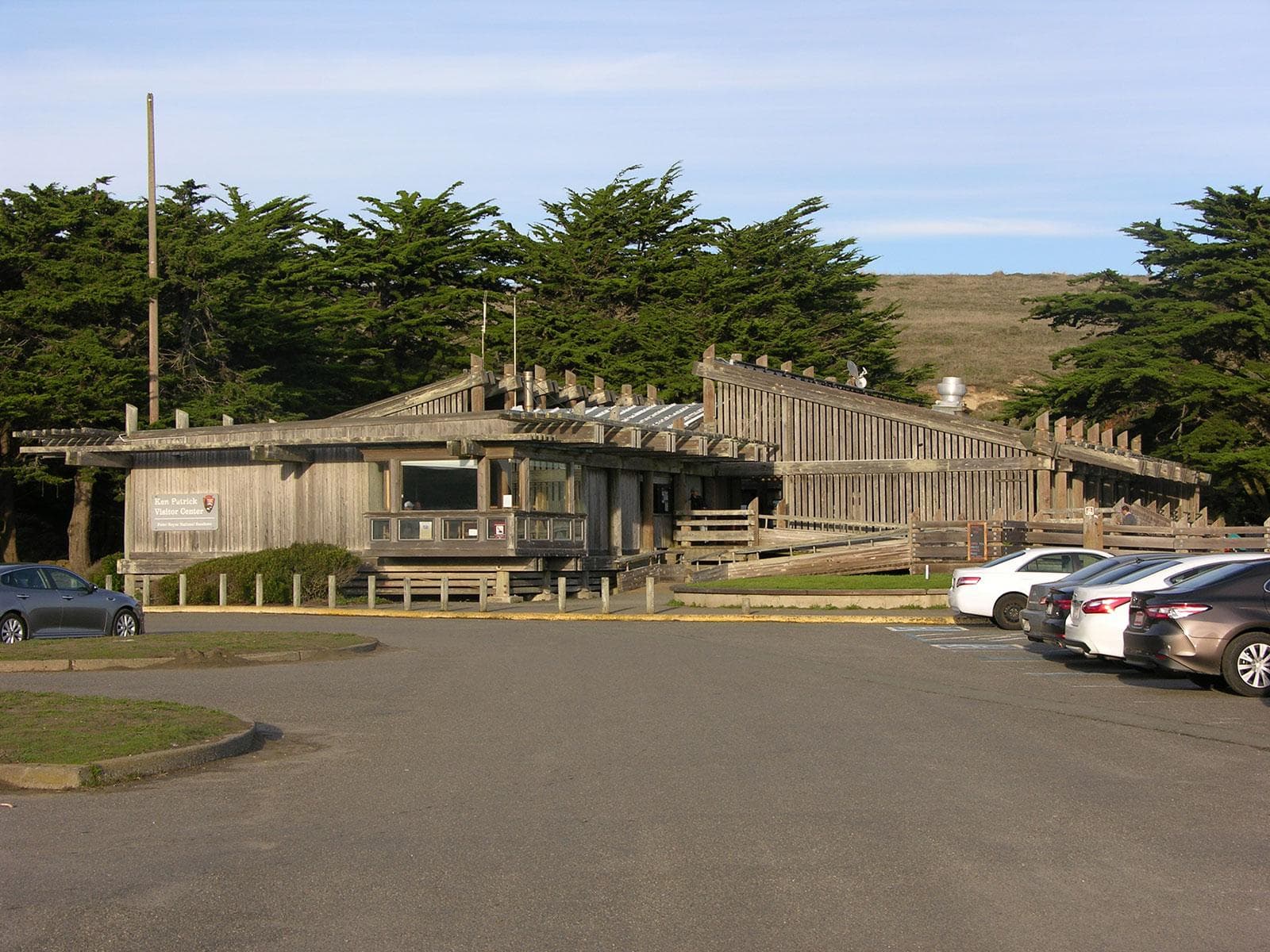 A moderately sized brown wooden structure with slanted rooflines beyond a parking lot.