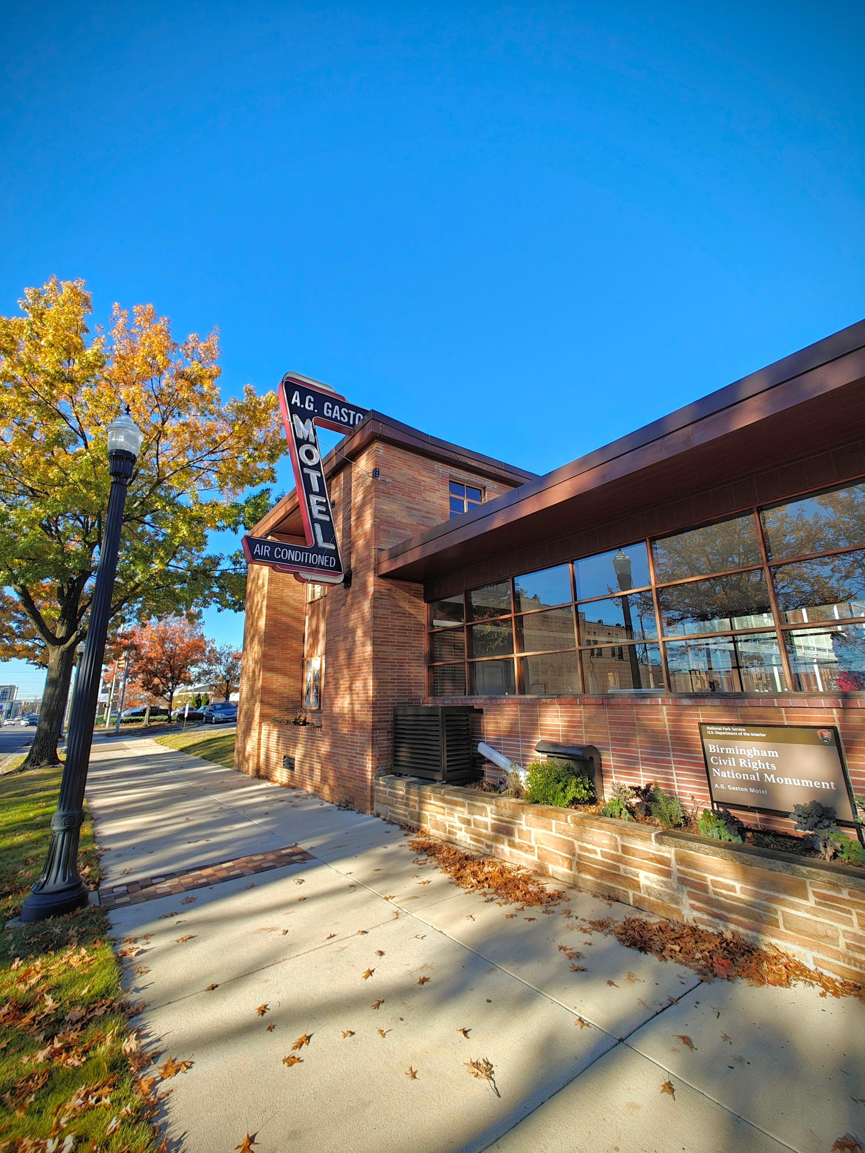 A brick and glass motel with fall leaves. A neon sign saying A.G. Gaston Motel is on the wall.