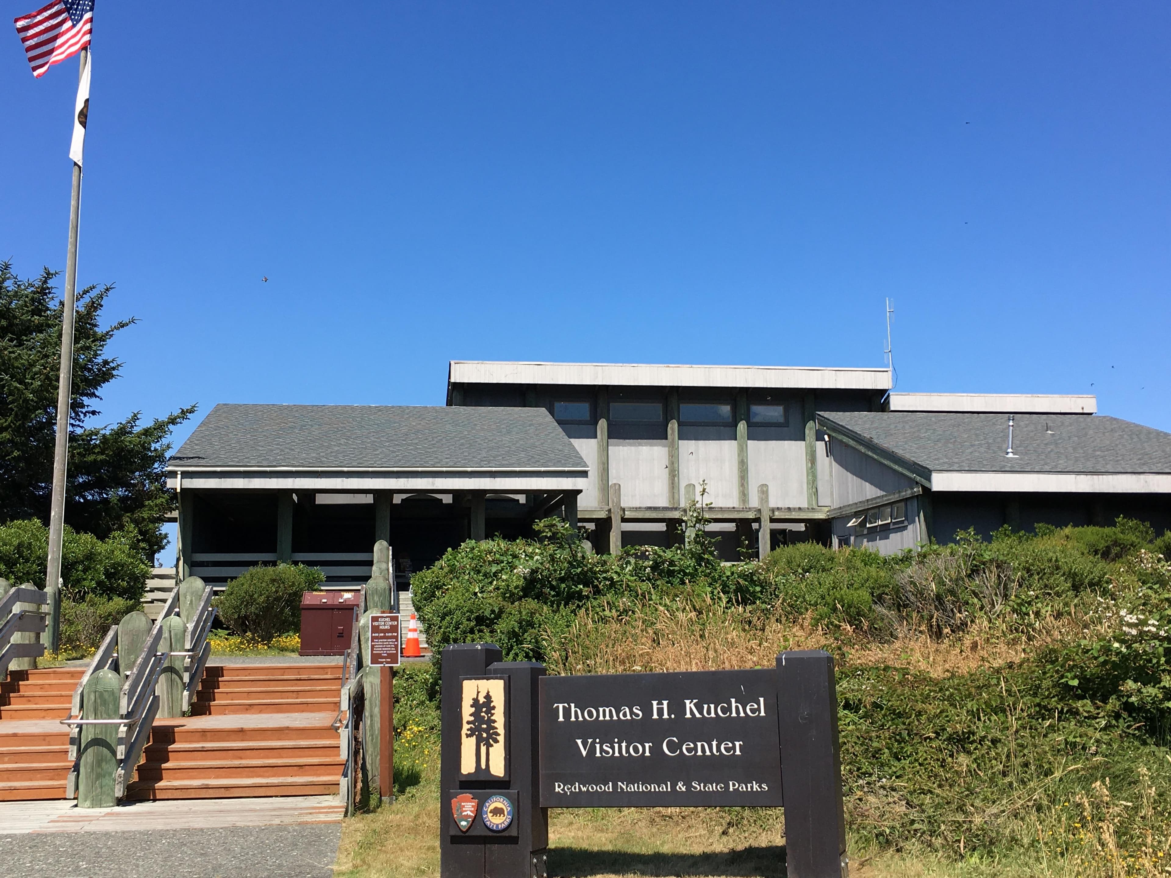 A brown and grey visitor center with a flagpole flying the US and California flags..