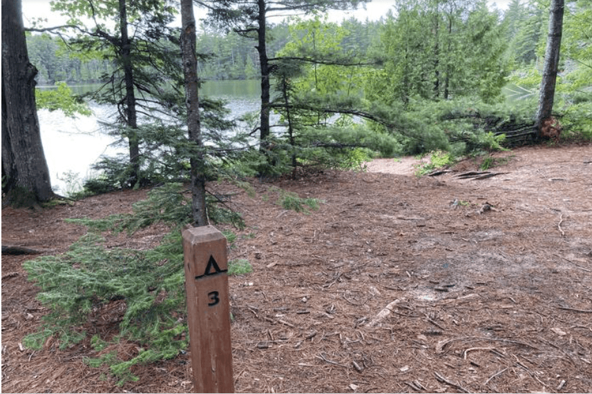 Cleared campsite with a lake in the background visible between a few trees.
