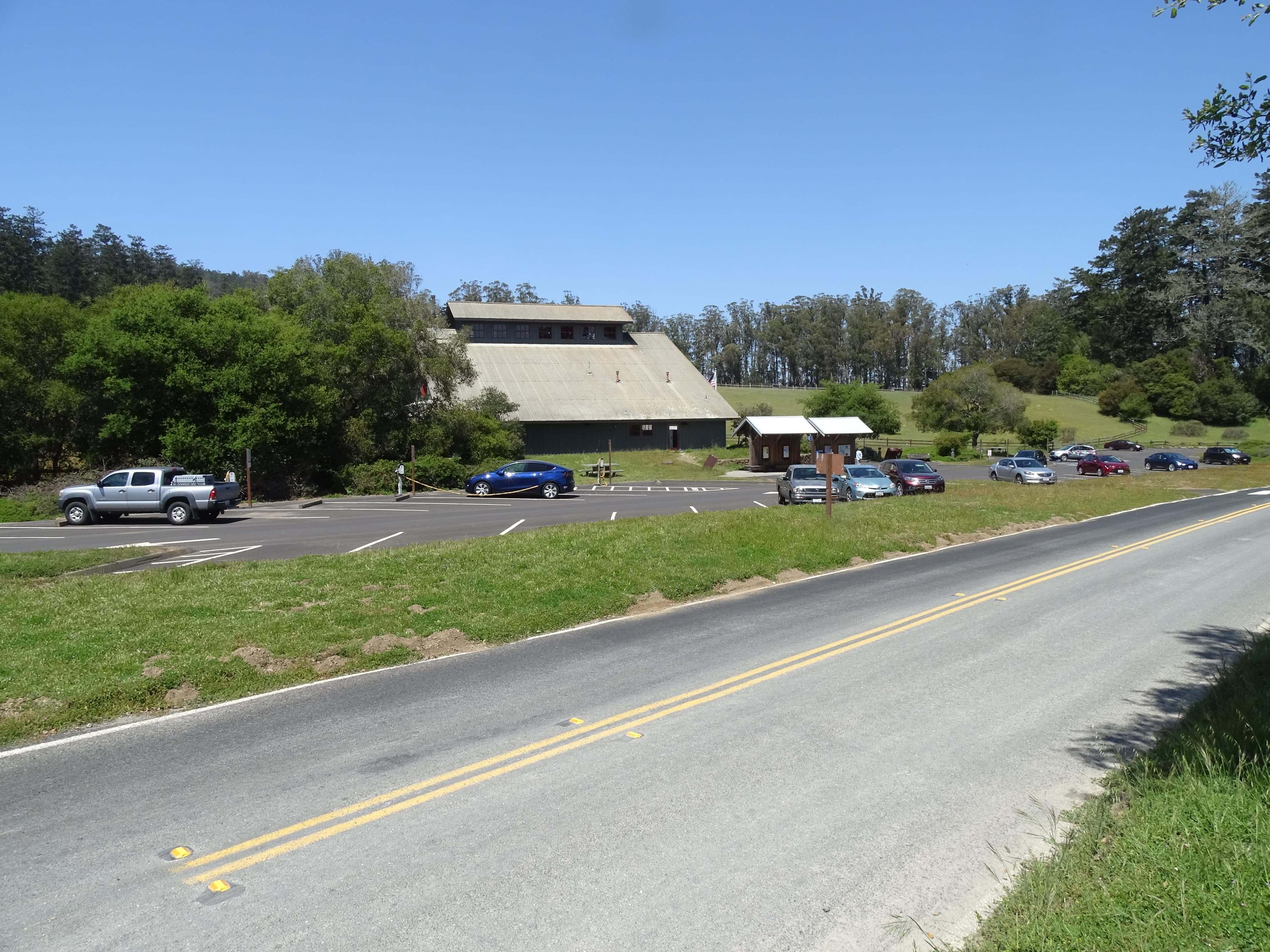 Several vehicles parked in a paved parking lot with a gray barn-like structure in the background.