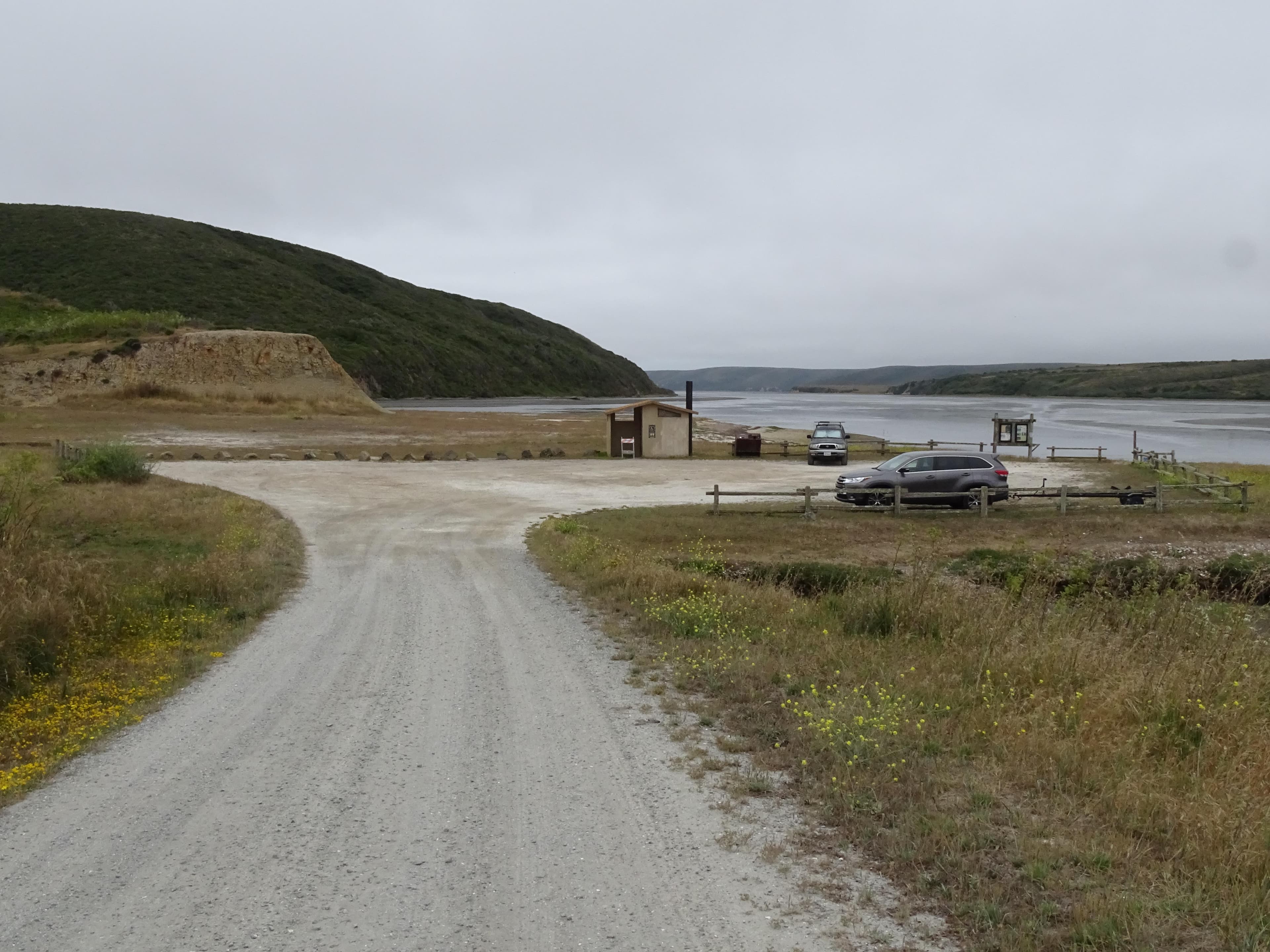 Two vehicles in a small, dirt parking lot adjacent to an estuary on the right.