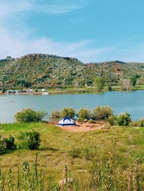 Camping in meadow by Harbor Bay. There are mesas in the background and the lake and sky are blue.