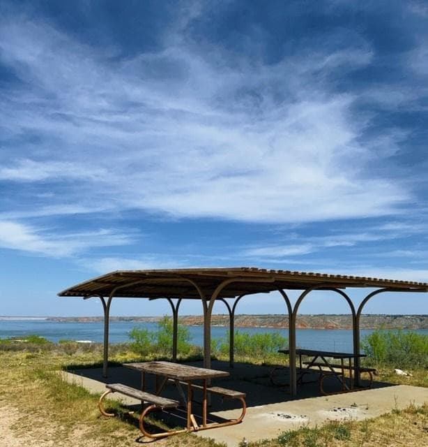 A picnic area at Blue West overloooking the lake. The sky is blue with white clouds.