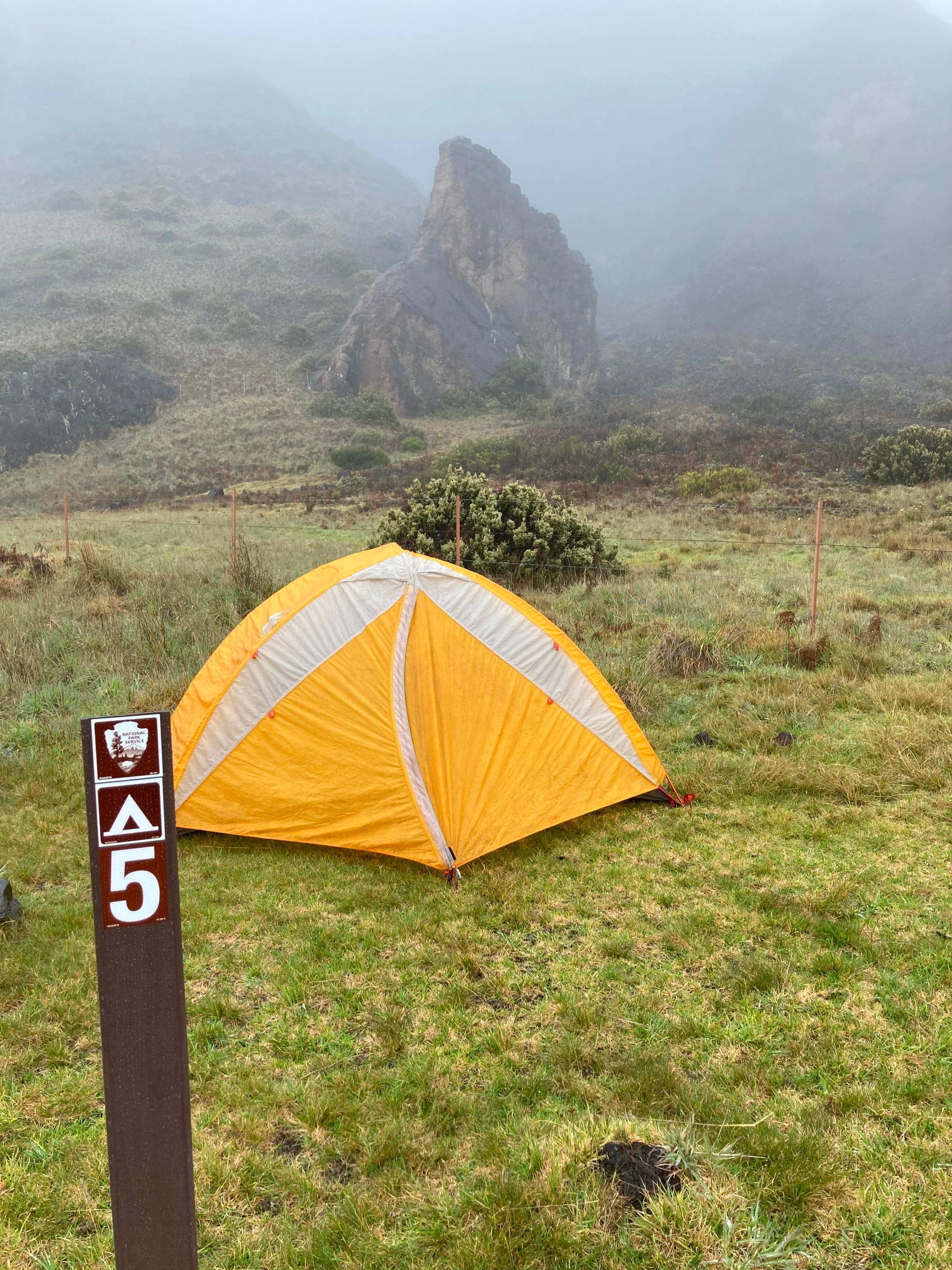 orange tent set up in grassy area with mist and clouds in background