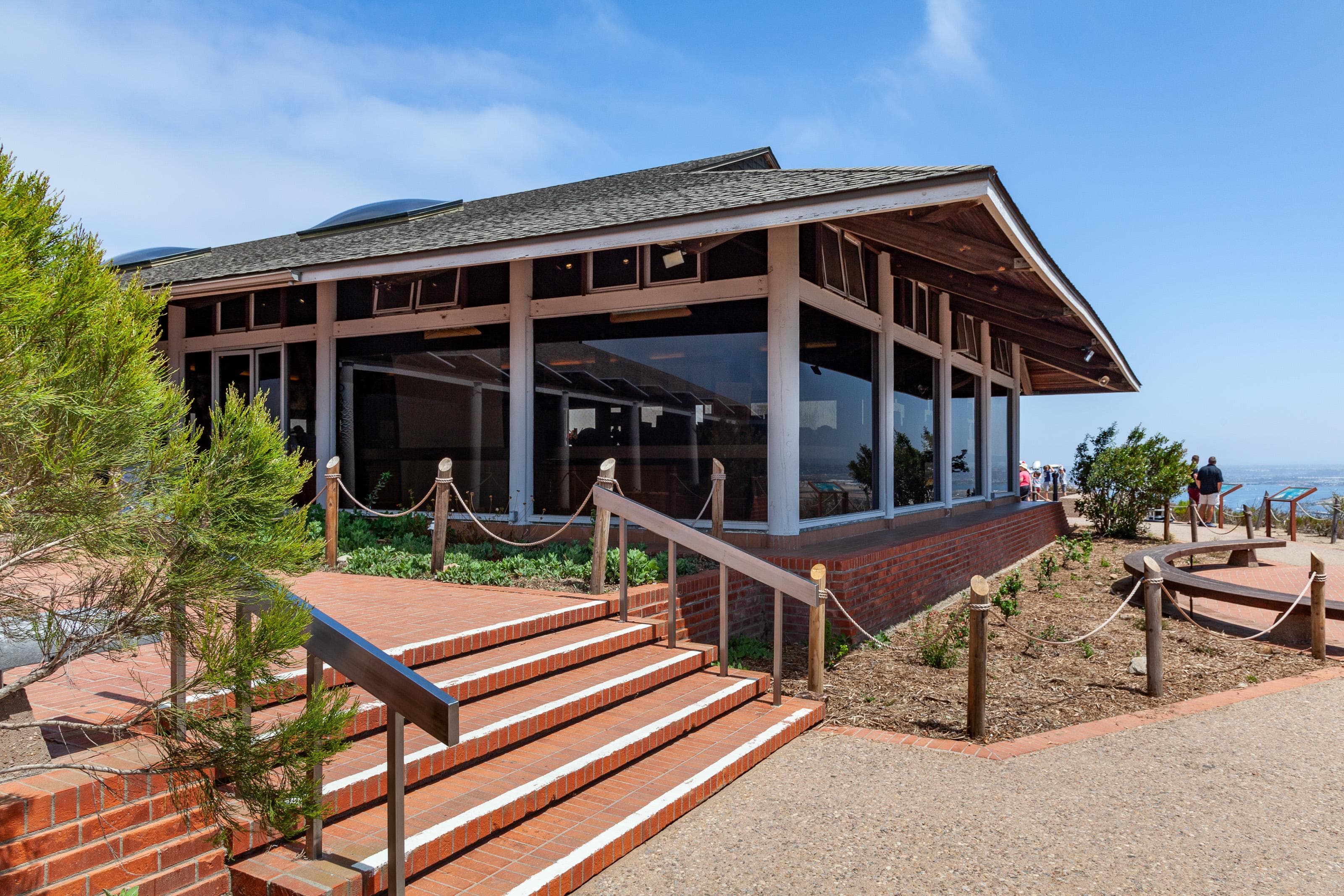A one story building with floor to ceiling windows. Brick steps descending to a stone walkway is in