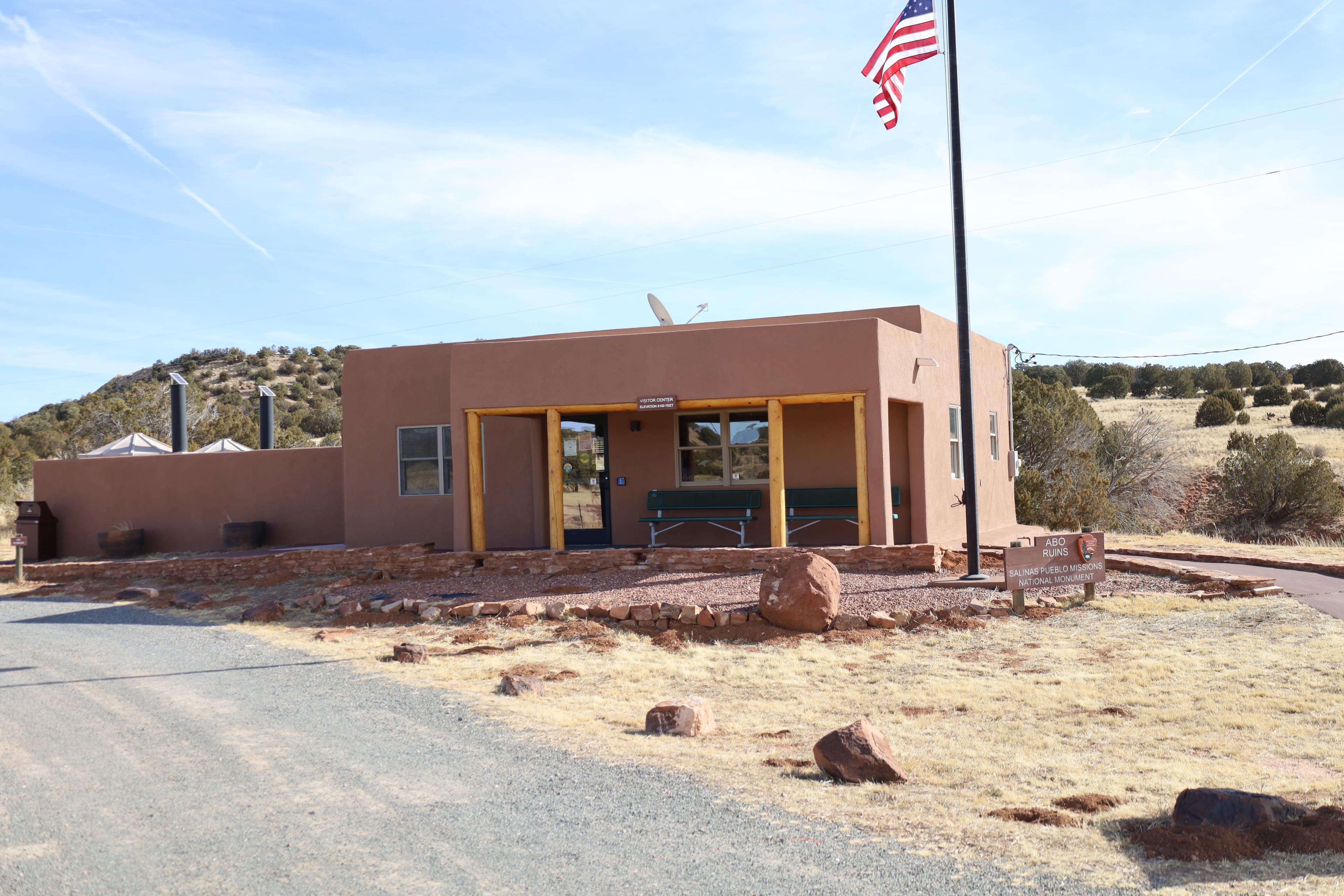 A square, brown building with two green benches on the front porch.