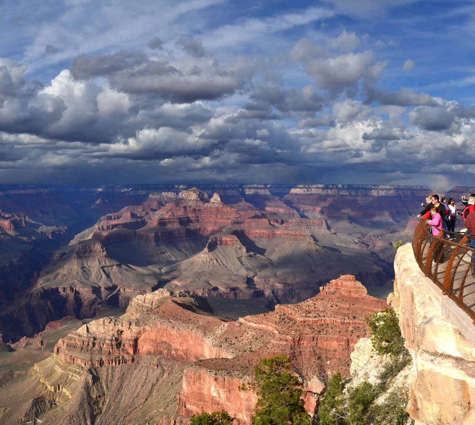 A small group of people look out over Grand Canyon from behind a metal railing