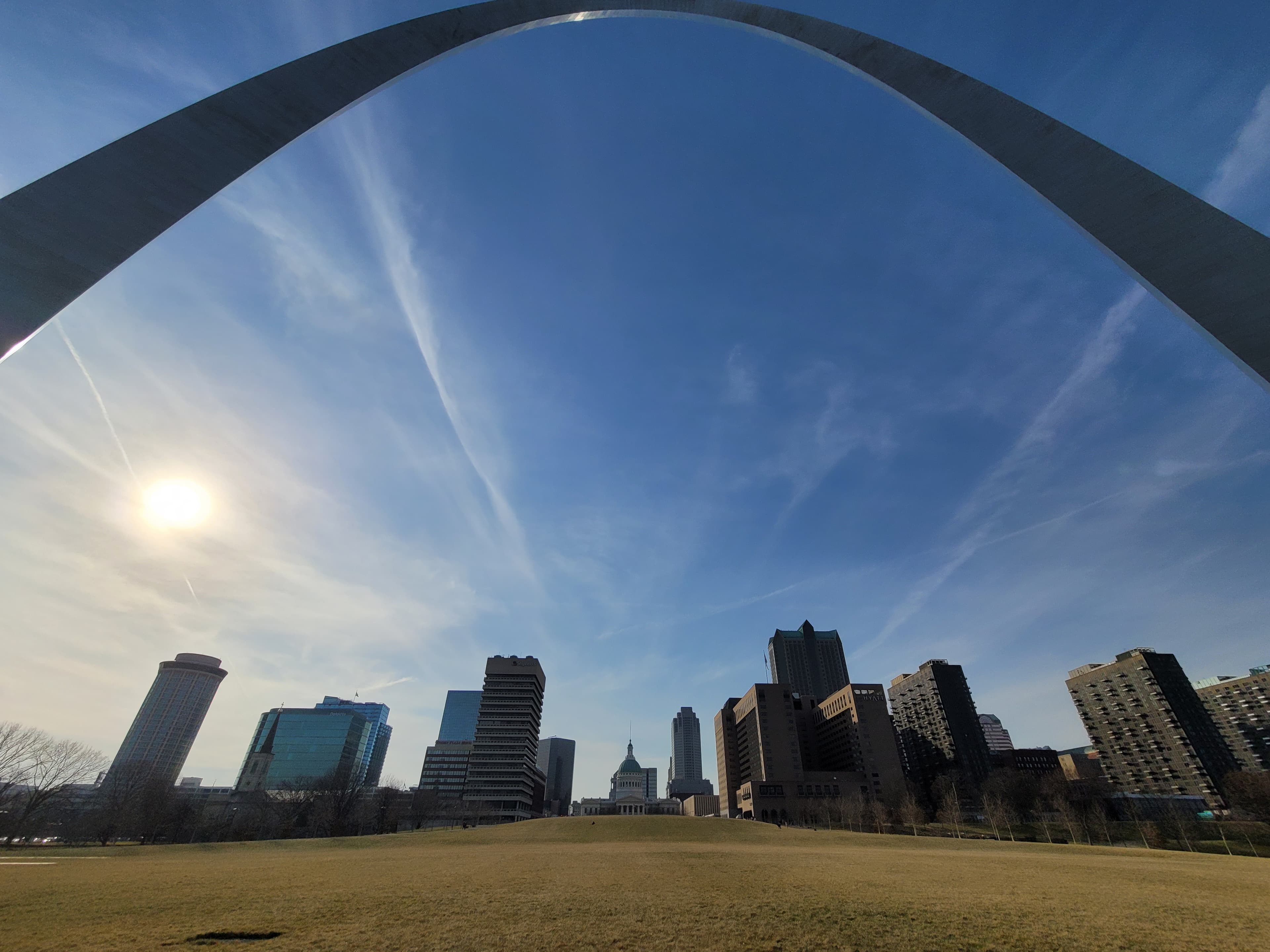 looking up at the curve of the Gateway Arch from below and the city buildings against a blue sky