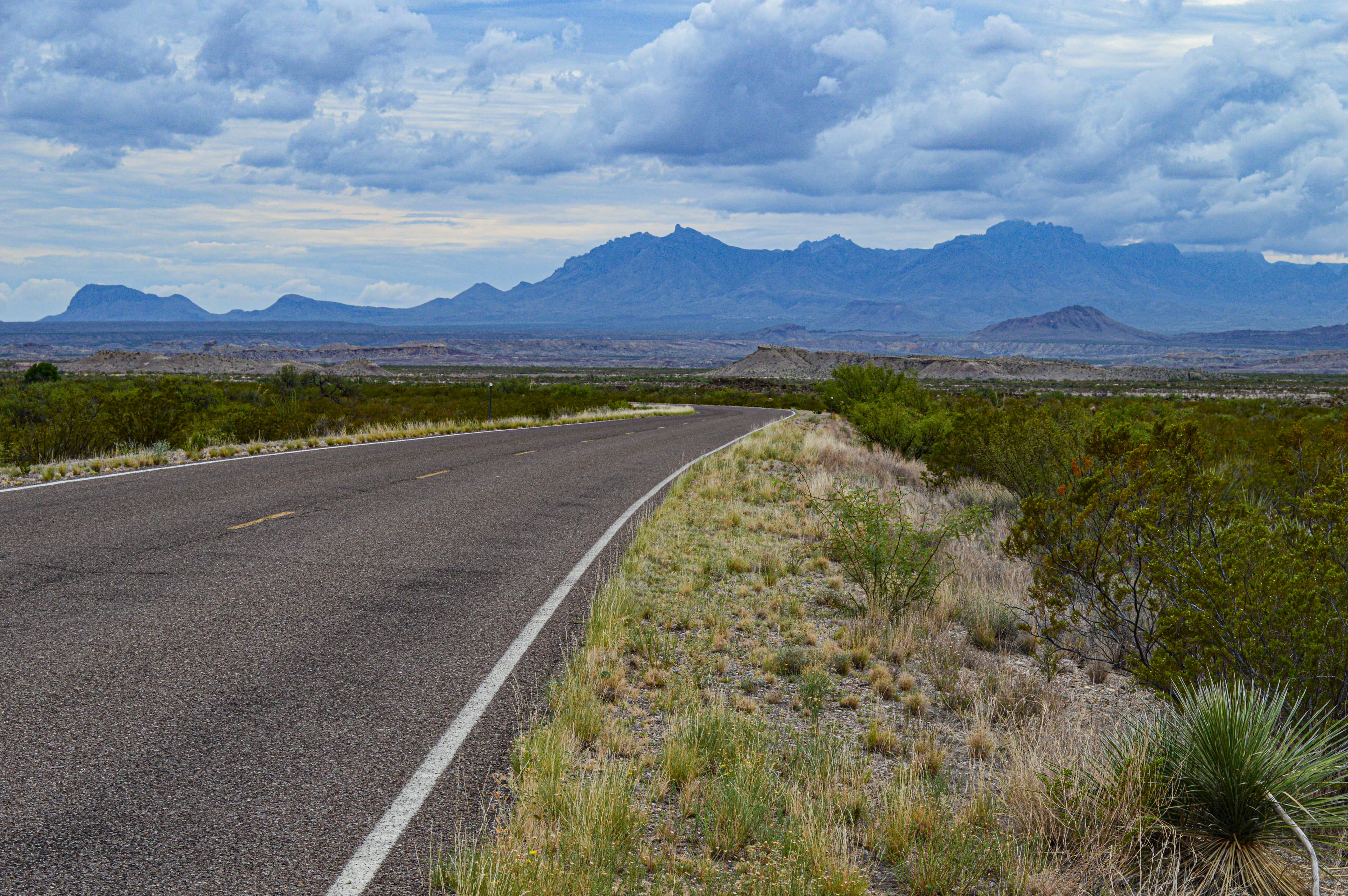 A paved road heads in a straight line through the desert towards a distant line of mountains.