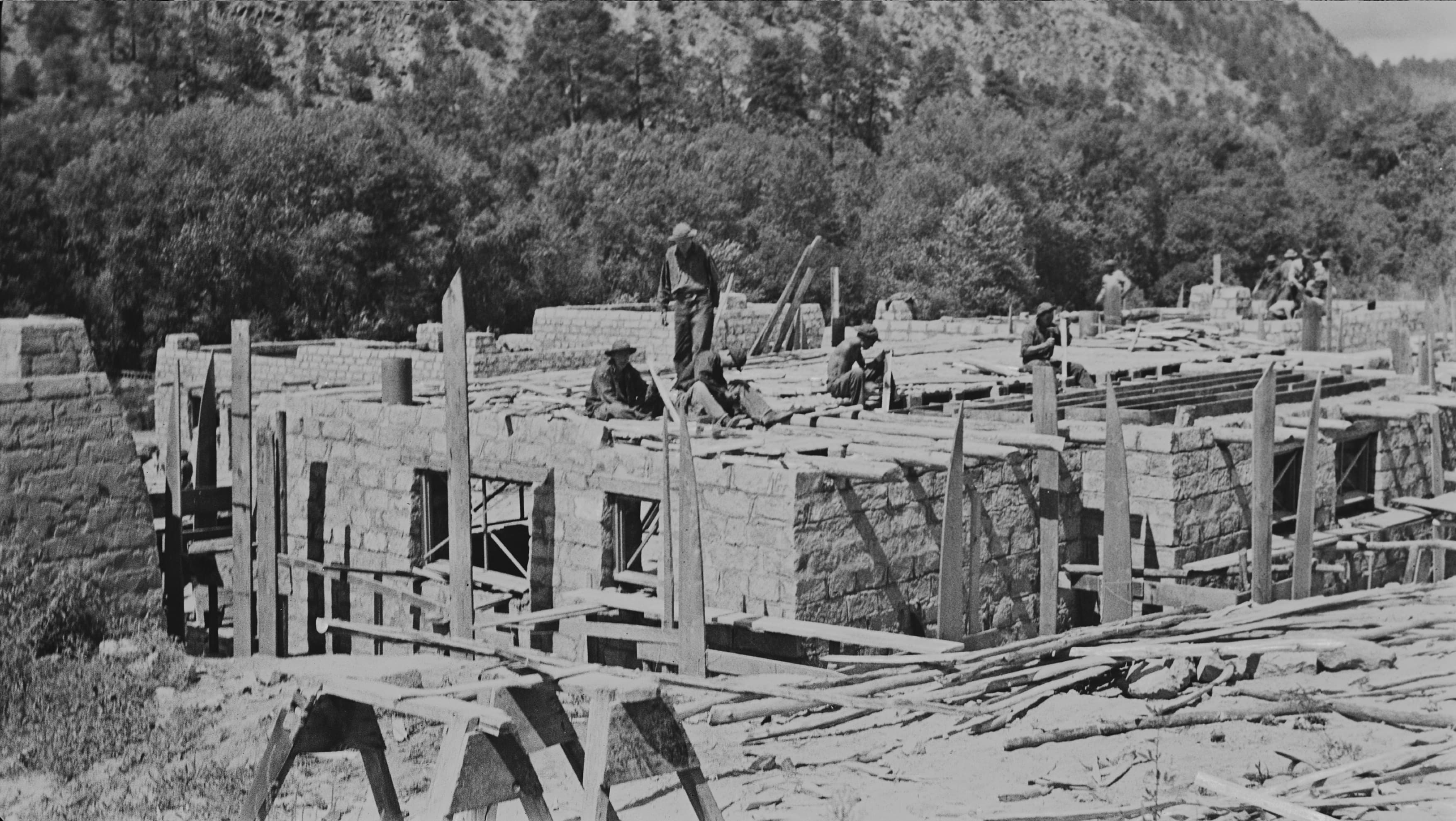 a stone building is under construction, men are working on the roof