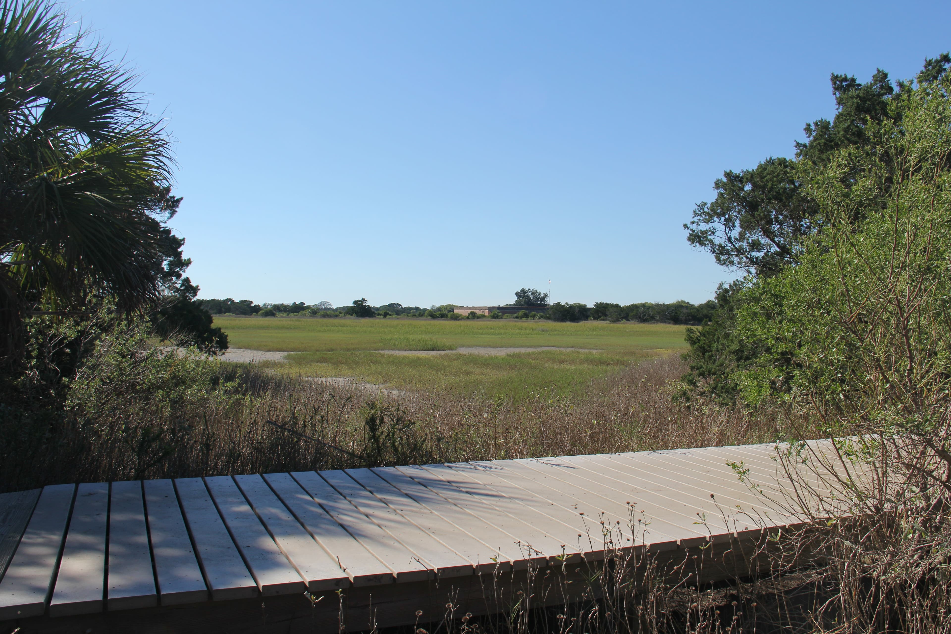 A boardwalk over a marsh with a large brick fort in the distance.