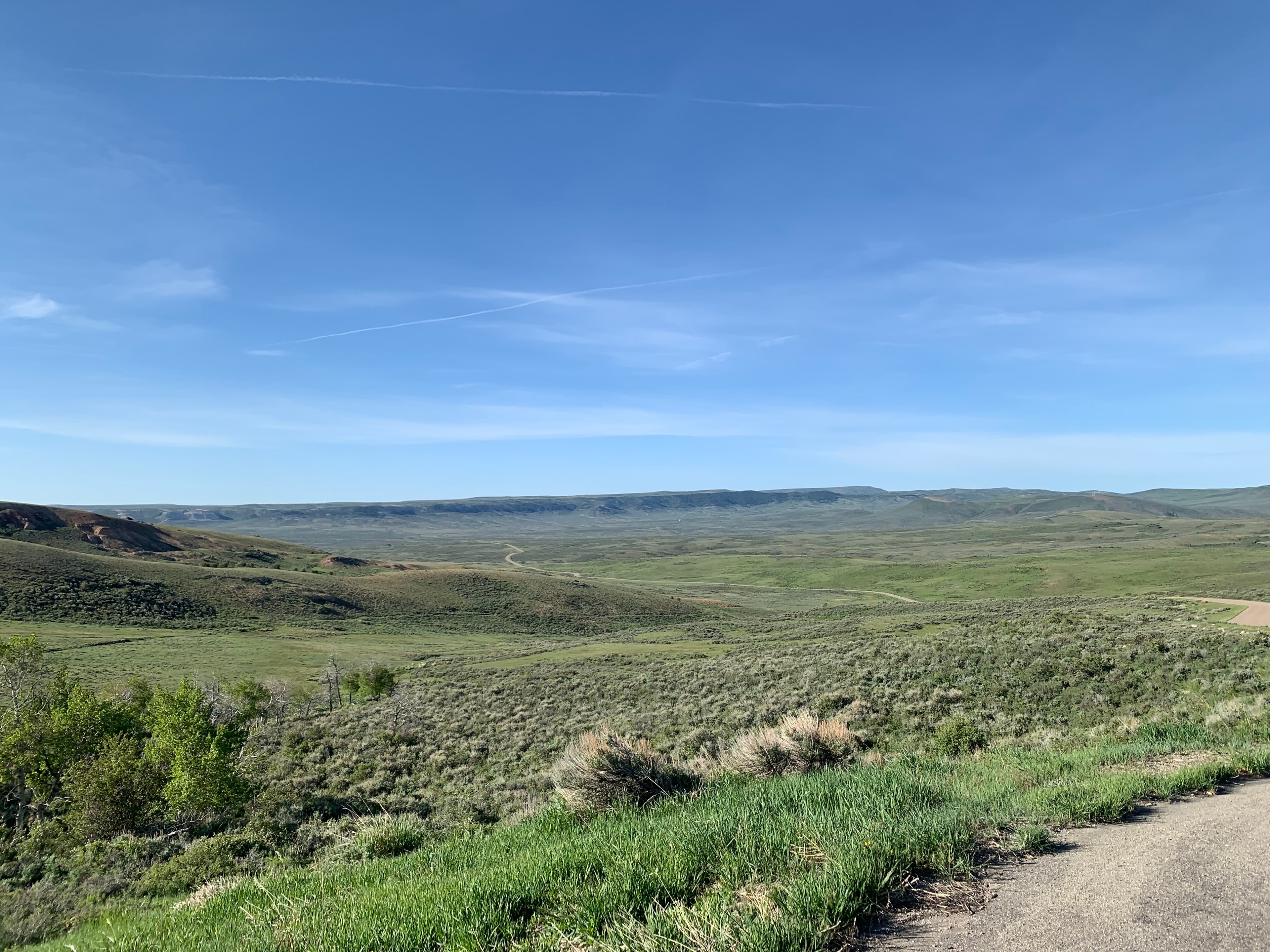 The road leads away through mildly rolling hills of sagebrush and green grasses.