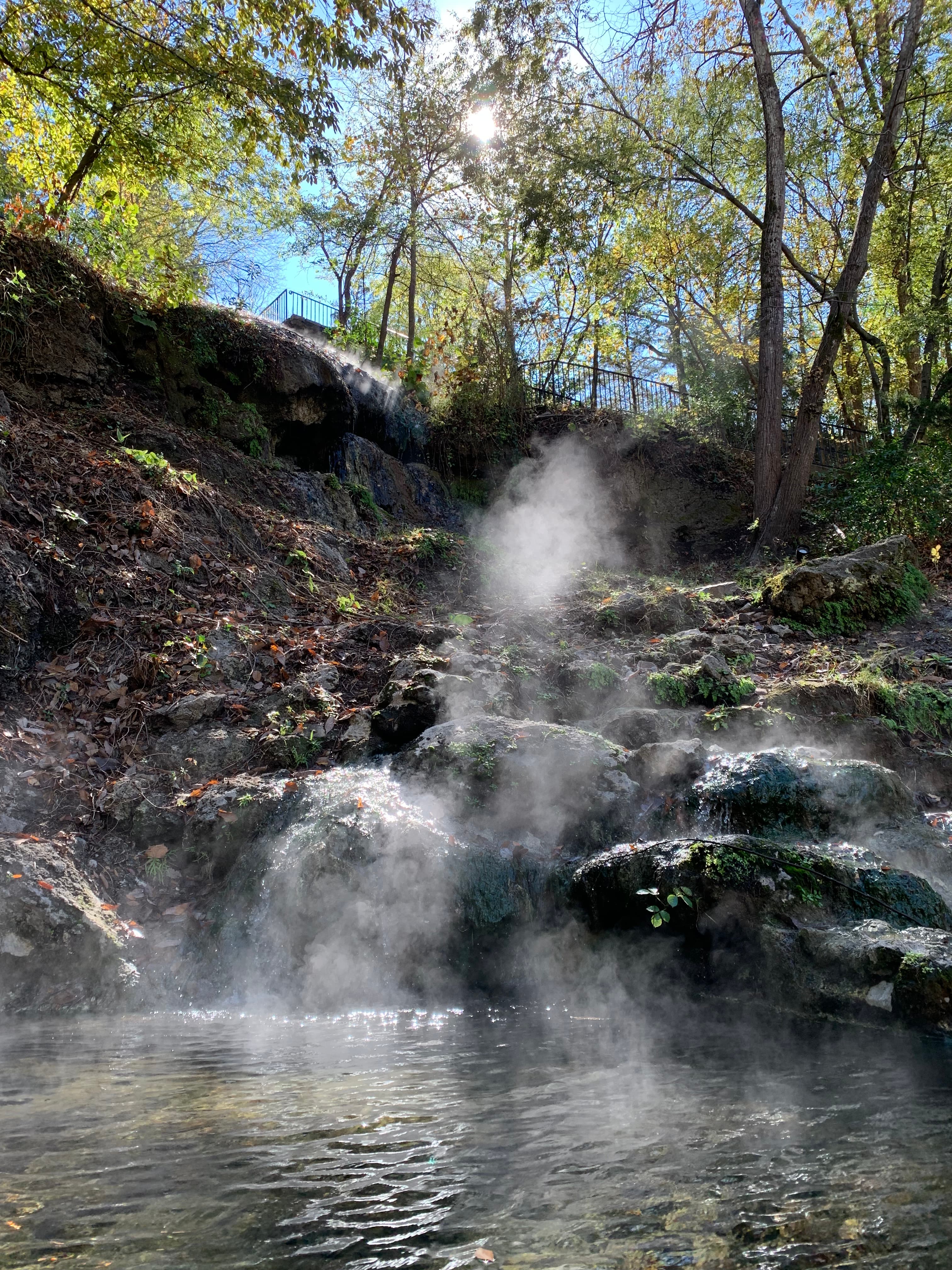 Sunlight shines on the steam of a small waterfall of hot water.