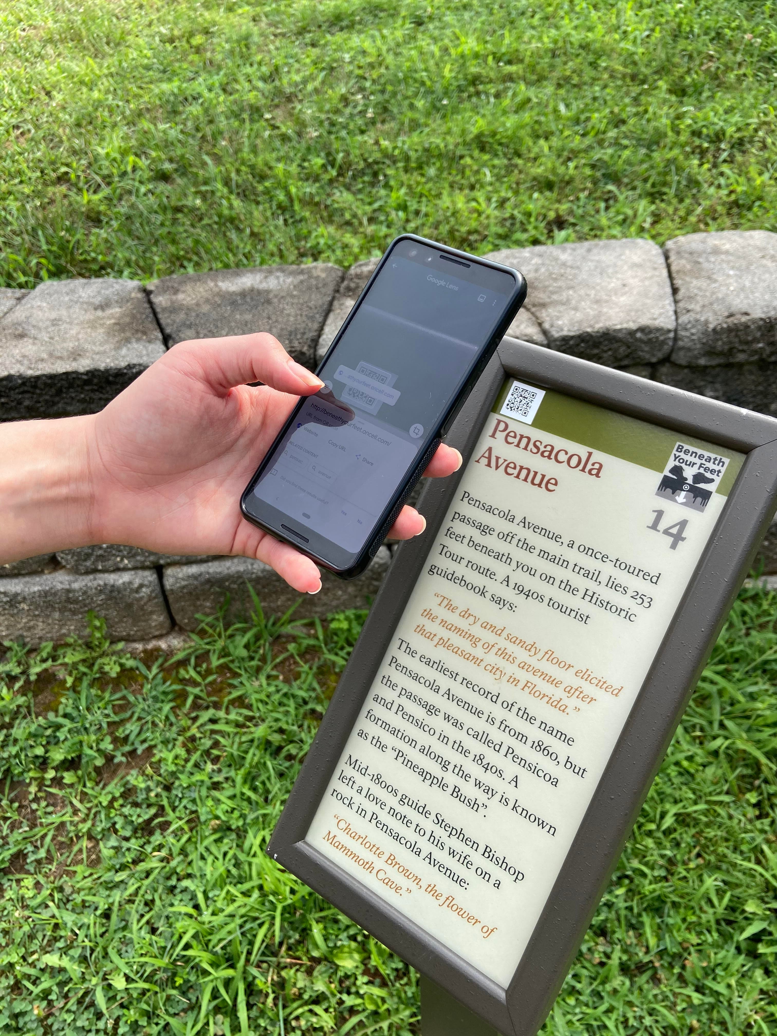 A person holding a smart phone near a wayside sign.